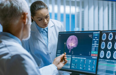 Two Medical Scientists in the Brain Research Laboratory Discussing Progress on the Neurophysiology Project Fighting Tumors. Neuroscientists Use Personal Computer with MRI, CT Scans Show Brain Images.