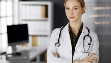 Cheerful smiling female doctor standing in clinic. Portrait of friendly physician woman. Perfect medical service in hospital. Medicine concept.