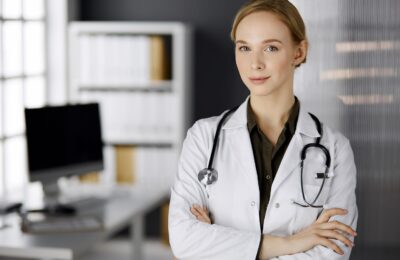 Cheerful smiling female doctor standing in clinic. Portrait of friendly physician woman. Perfect medical service in hospital. Medicine concept.