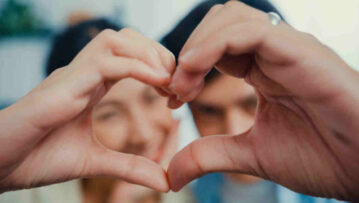 Close-up Young Asian married couple with casual sitting on couch make hand to be love sign heart shape and looking at camera with sweet and happy moment in living room at home.