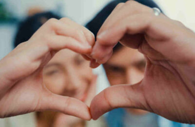 Close-up Young Asian married couple with casual sitting on couch make hand to be love sign heart shape and looking at camera with sweet and happy moment in living room at home.