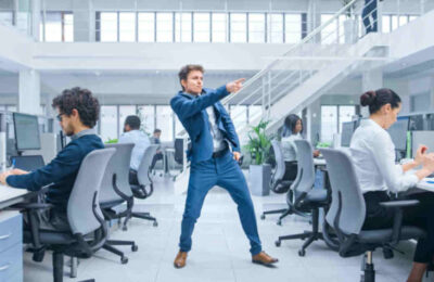 Young Cheerful Handsome Business Manager Wearing a Suit and Tie is Dancing like Crazy in the Office. Diverse and Motivated Business People Work on Computers in Modern Open Office.