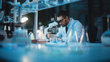 Medical Development Laboratory: Caucasian Female Scientist Looking Under Microscope, Analyzes Petri Dish Sample. Specialists Working on Medicine, Biotechnology Research in Advanced Pharma Lab